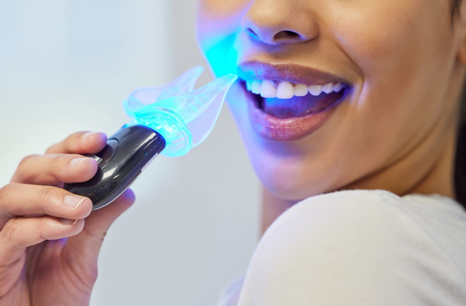 Close-up of a person using a handheld blue light device for Zoom teeth whitening